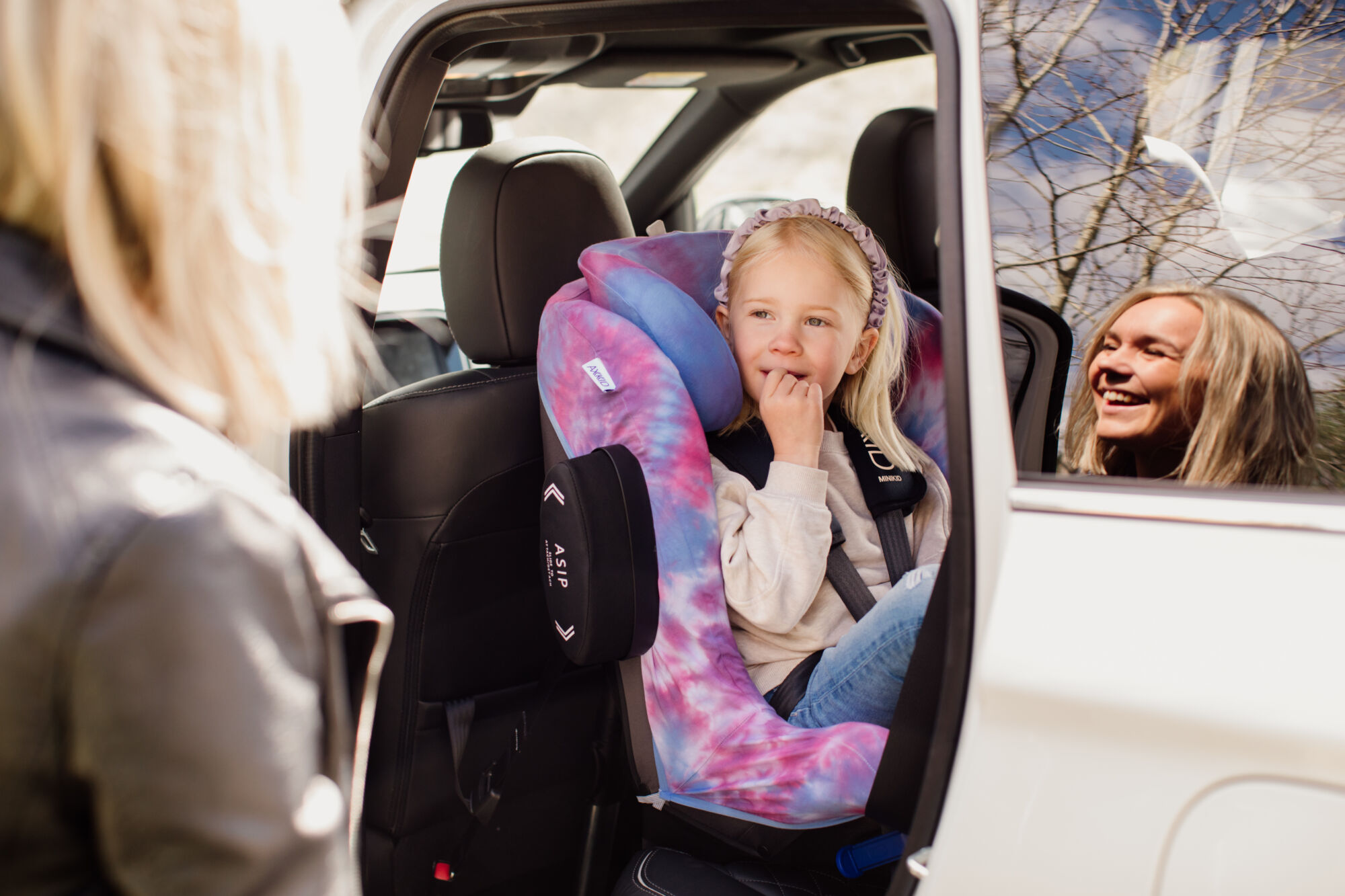 Girl sitting in rear facing car seat Axkid Minikid 2 with car seat cover on.