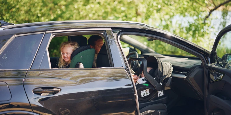 Picture of a car with the passenger door open with a baby car seat. In the rear is a child in a rear facing car seat.