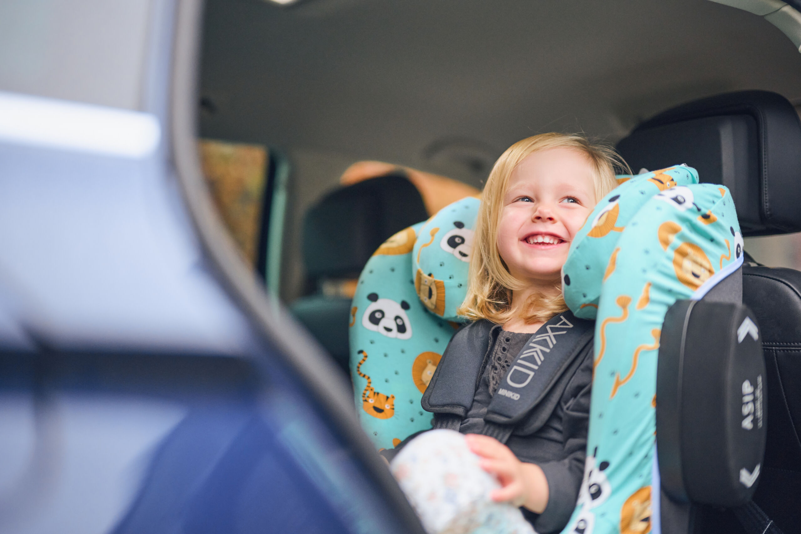 Child sitting in car seat Axkid Minikid 2 with car seat cover from Axkid x Geggamoja.