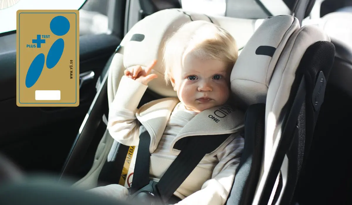golden plus test symbol on the left side of the picture, a boy sitting in a rear facing car seat looking at the camera on the right side of the picture