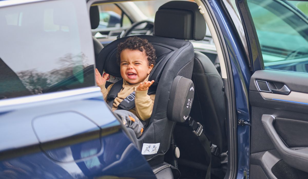 toddler with his hands up in the air sitting in a car seat facing backwards