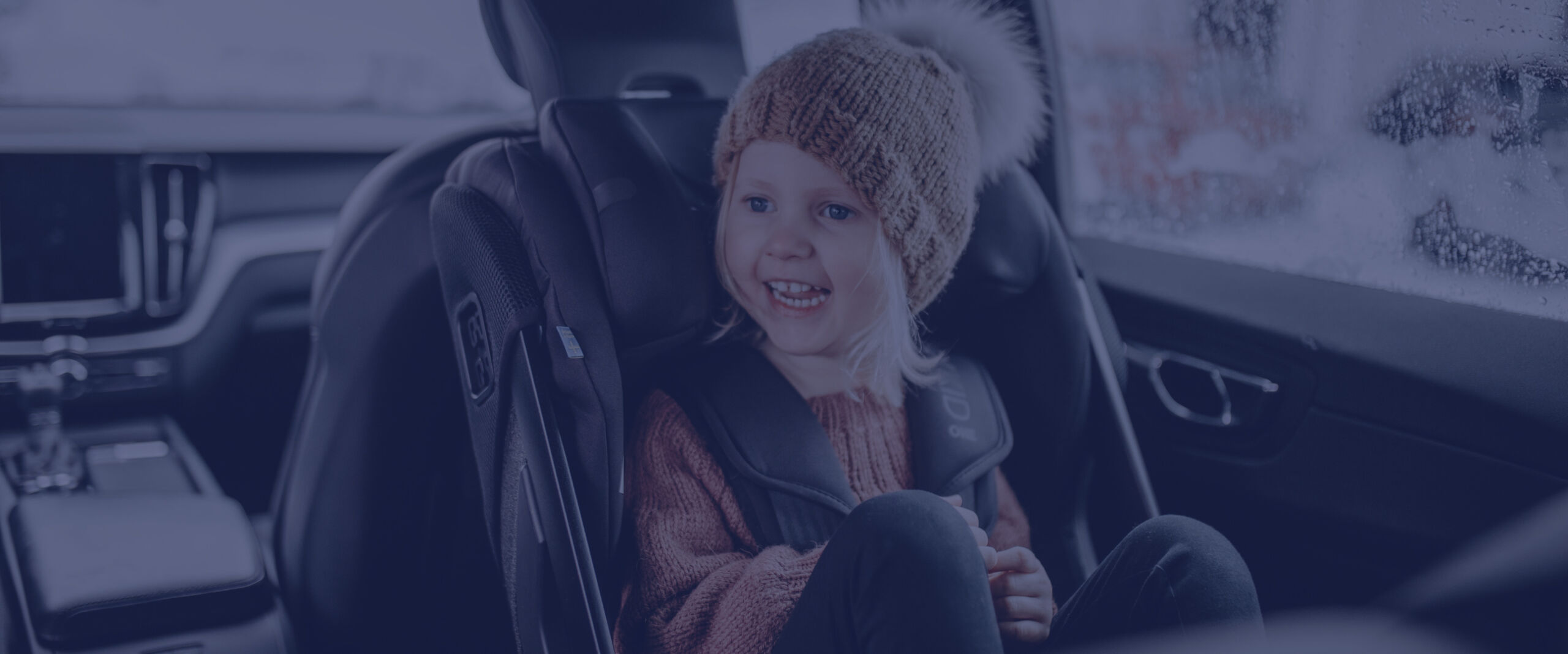toddler in winter hat sitting rear facing in Axkid car seat